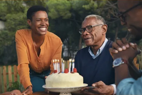 Actor portrayals of a woman presenting her father a birthday cake, outside with family