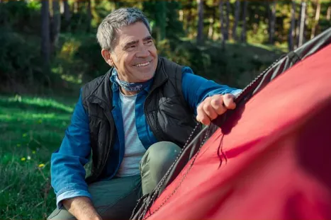 Actor portrayal of a man holding a tent and smiling